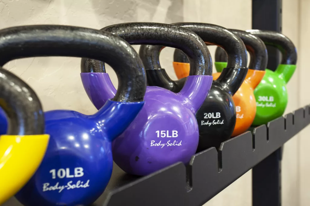 Colorful kettlebells in varying weights are lined up on a rack, labeled from 10LB to 30LB.