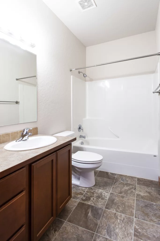 A bathroom with a sink and vanity, toilet, and a shower-tub combo, featuring white walls and tile flooring.
