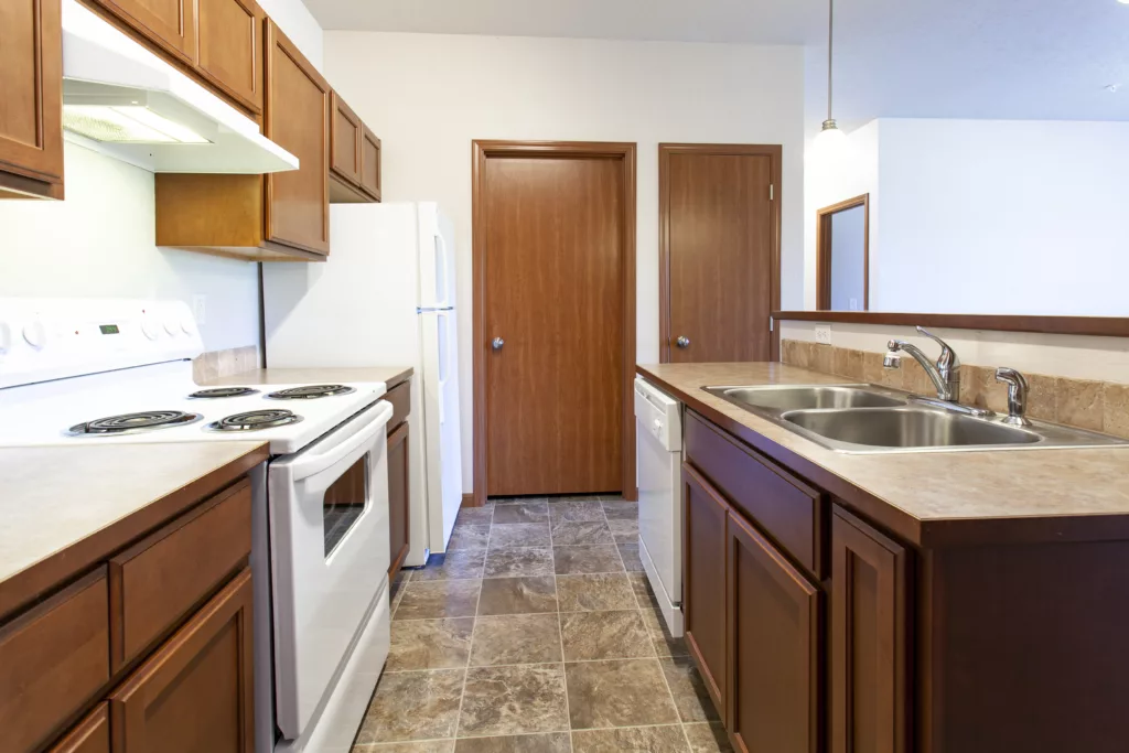 Kitchen with wooden cabinets, white appliances, double sink, and tiled floor.