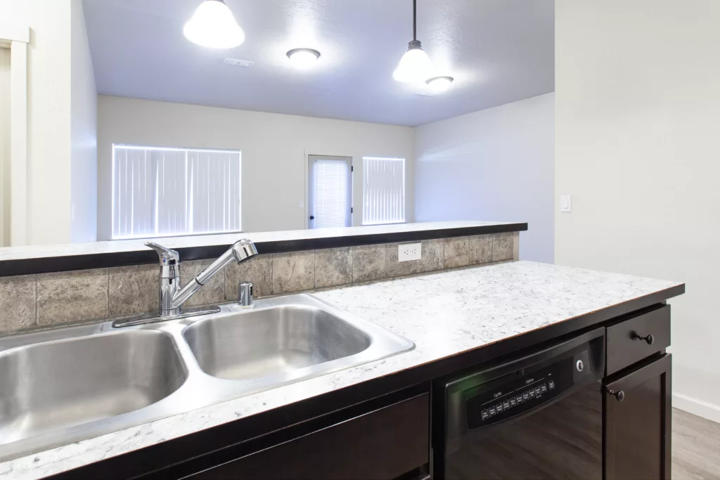 A modern kitchen featuring a marble countertop with a double sink and dark cabinetry, under bright ceiling lights.