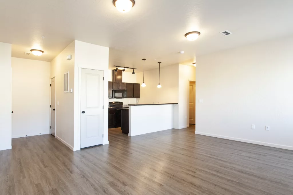 An unfurnished open-concept room with wood flooring, recessed lighting, and a kitchen area featuring dark cabinets and a breakfast bar.
