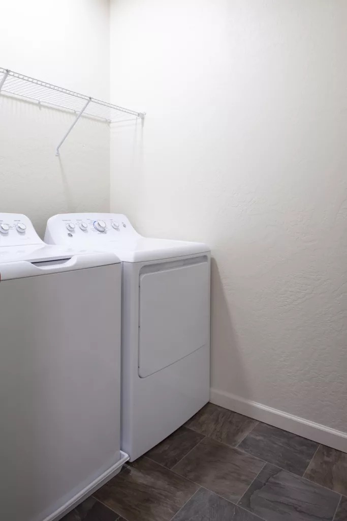 Washing machine and dryer in a laundry room with a simple wire shelf above them.